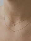 Two solid gold necklaces with lock and heart pendants on a person's neck.