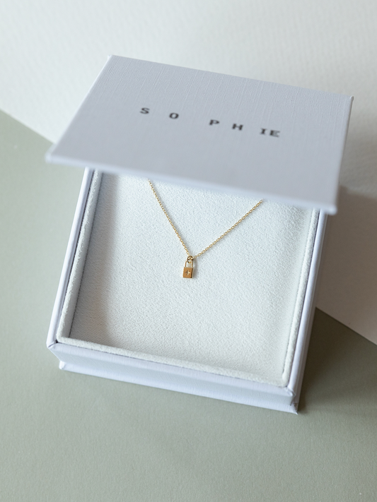 Solid gold little lock necklace in a white box with 'SOPHIE' branding on a light background