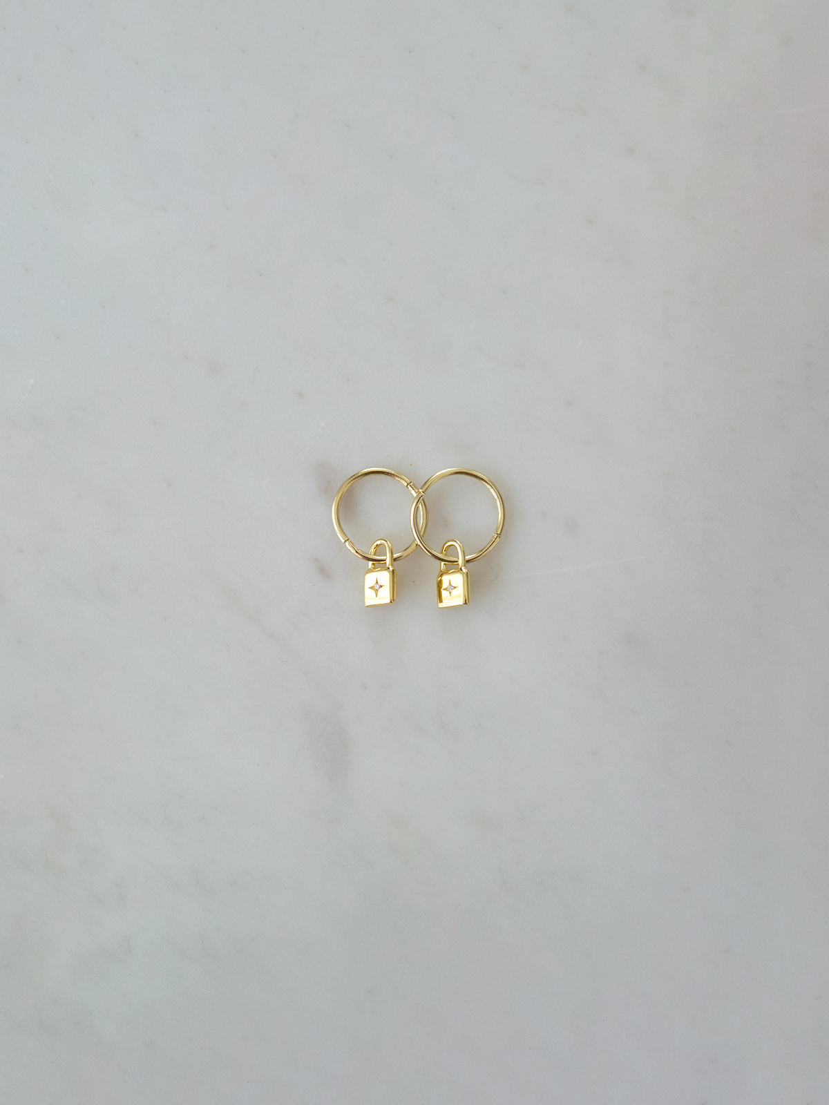Gold hoop earrings with small padlock charms with a zircon stone on a light gray background