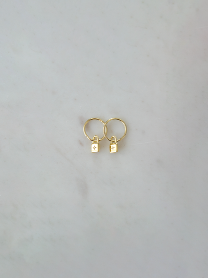 Gold hoop earrings with small padlock charms with a zircon stone on a light gray background
