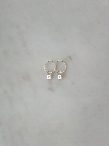 Pair of silver hoop earrings with a padlock charm and zircon stone on a light gray background