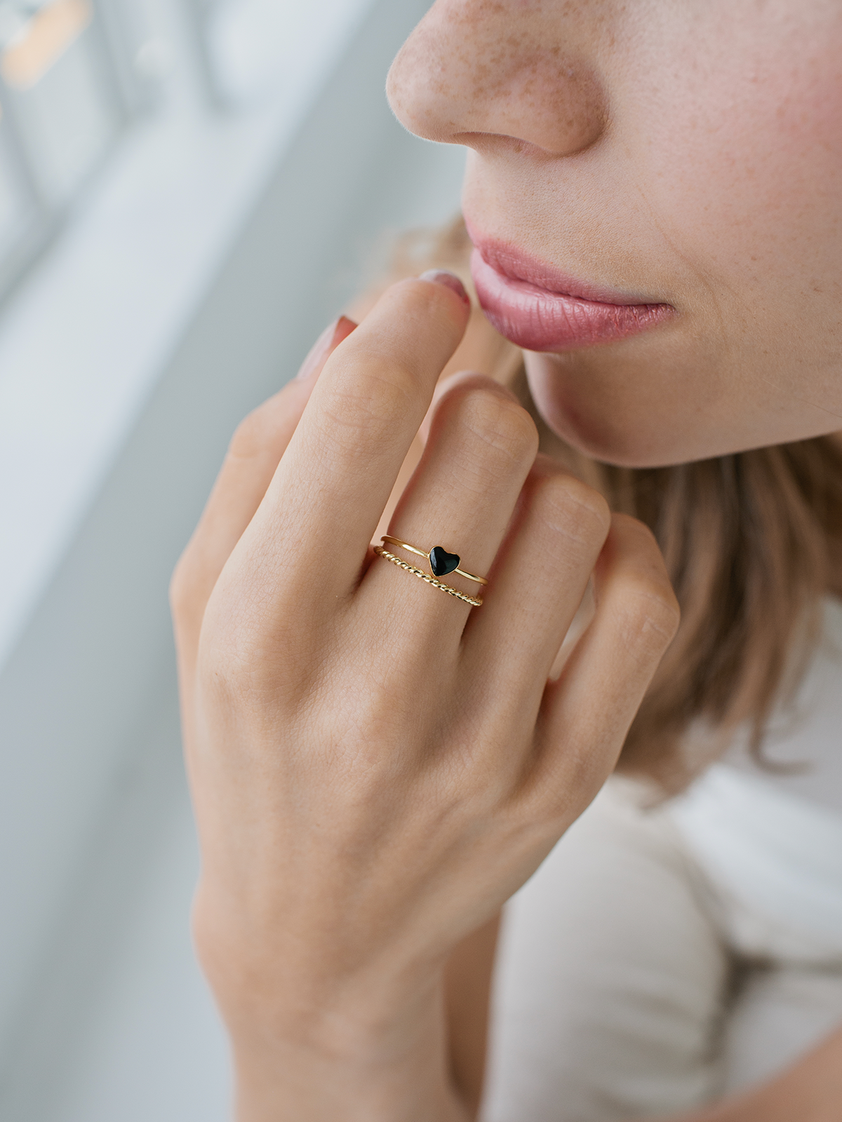 Close-up of a hand wearing a gold ring with a black heart stone, against a blurred background.