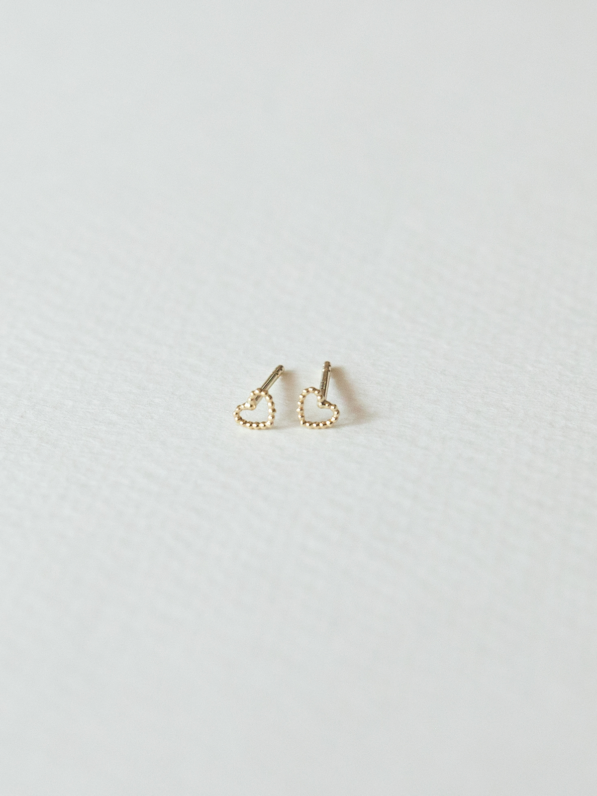 Solid gold dotty love heart-shaped stud earrings on a light gray background