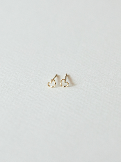 Solid gold dotty love heart-shaped stud earrings on a light gray background