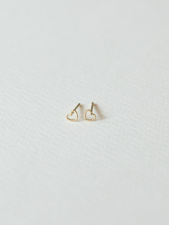 Solid gold dotty love heart-shaped stud earrings on a light gray background