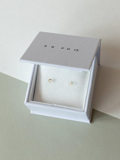 Solid gold dotty love heart shaped stud earrings in a 'SOPHIE' branded box on a light surface