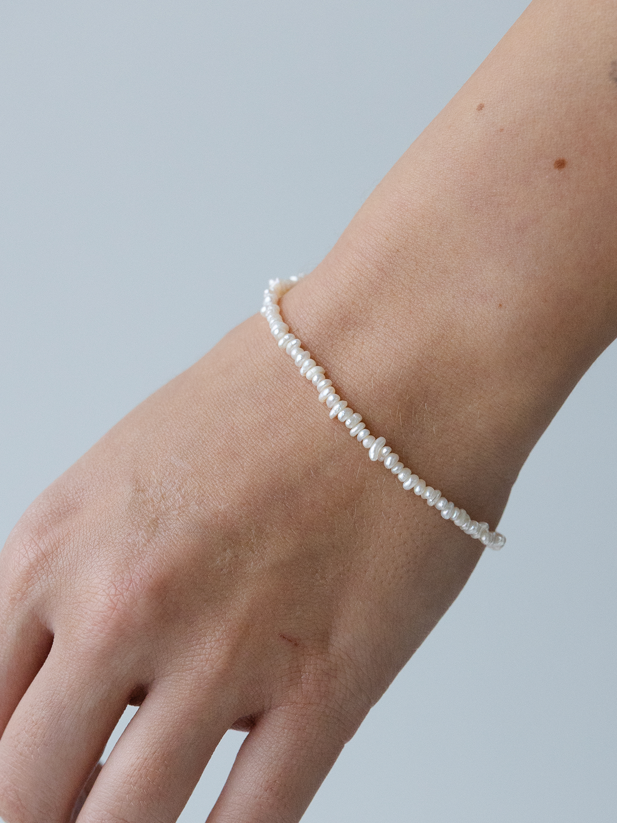 Pearl bracelet on a wrist against a light blue background
