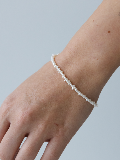 Pearl bracelet on a wrist against a light blue background