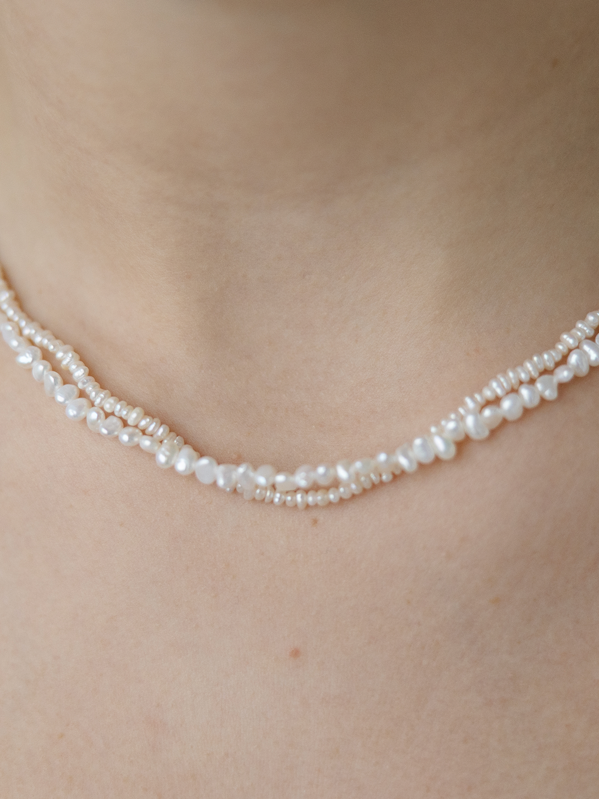 Pearl necklace on a person's neck against a neutral background