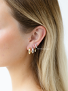 Close-up of a person's ear wearing gold hoop earrings with a plain background