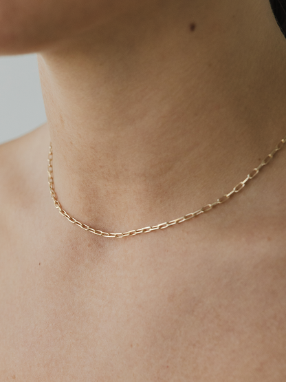 Gold chain necklace on a person's neck against a neutral background
