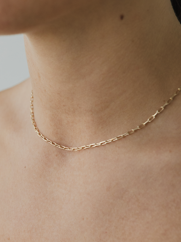 Gold chain necklace on a person's neck against a neutral background