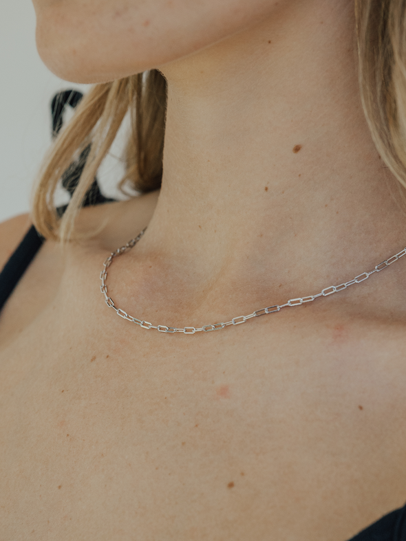 Close-up of a person wearing a delicate silver chain necklace.