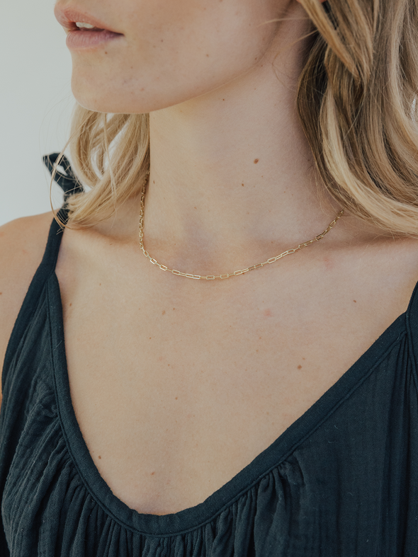 Woman wearing a gold necklace with a plain background