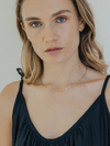 Woman wearing a black top and gold necklace against a neutral background