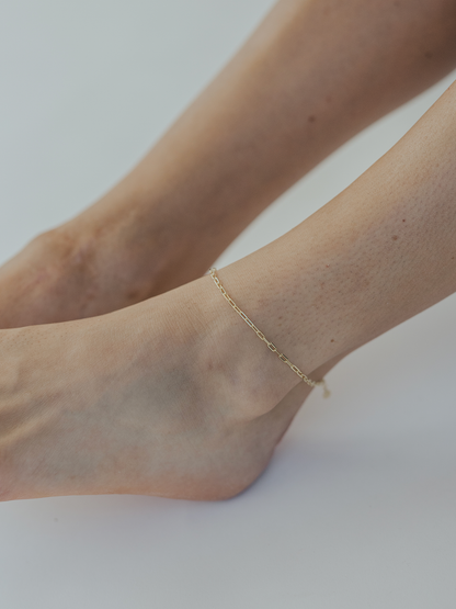 Gold anklet on a person's ankle against a white background