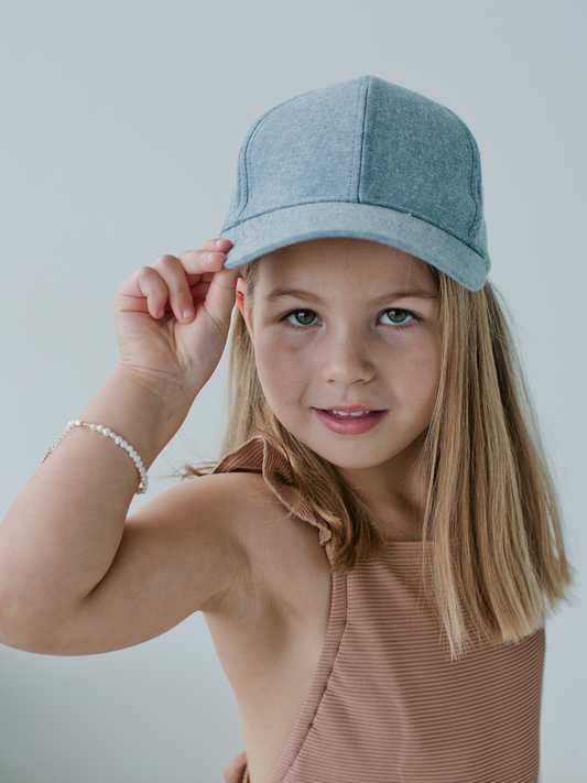 Young girl wearing a denim cap & mini pretty in pearls bracelet against a plain background