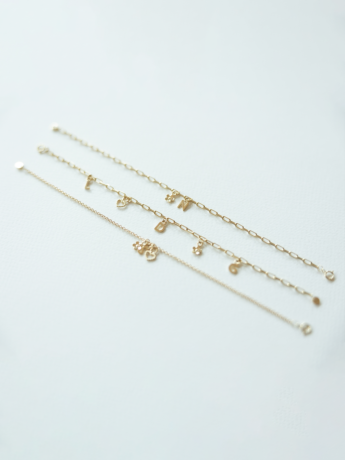 Three solid gold mix it up bracelets with various charms on a light gray background 