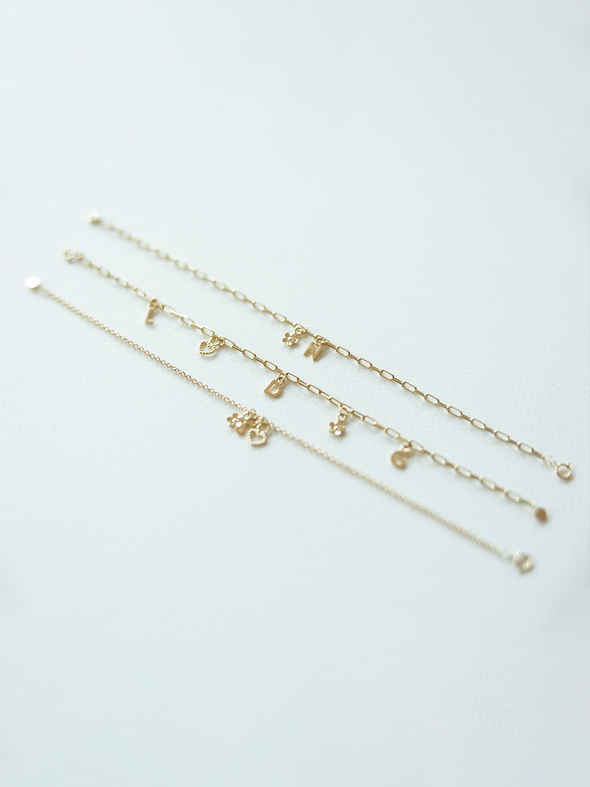 Three solid gold mix it up bracelets with various charms on a light gray background 