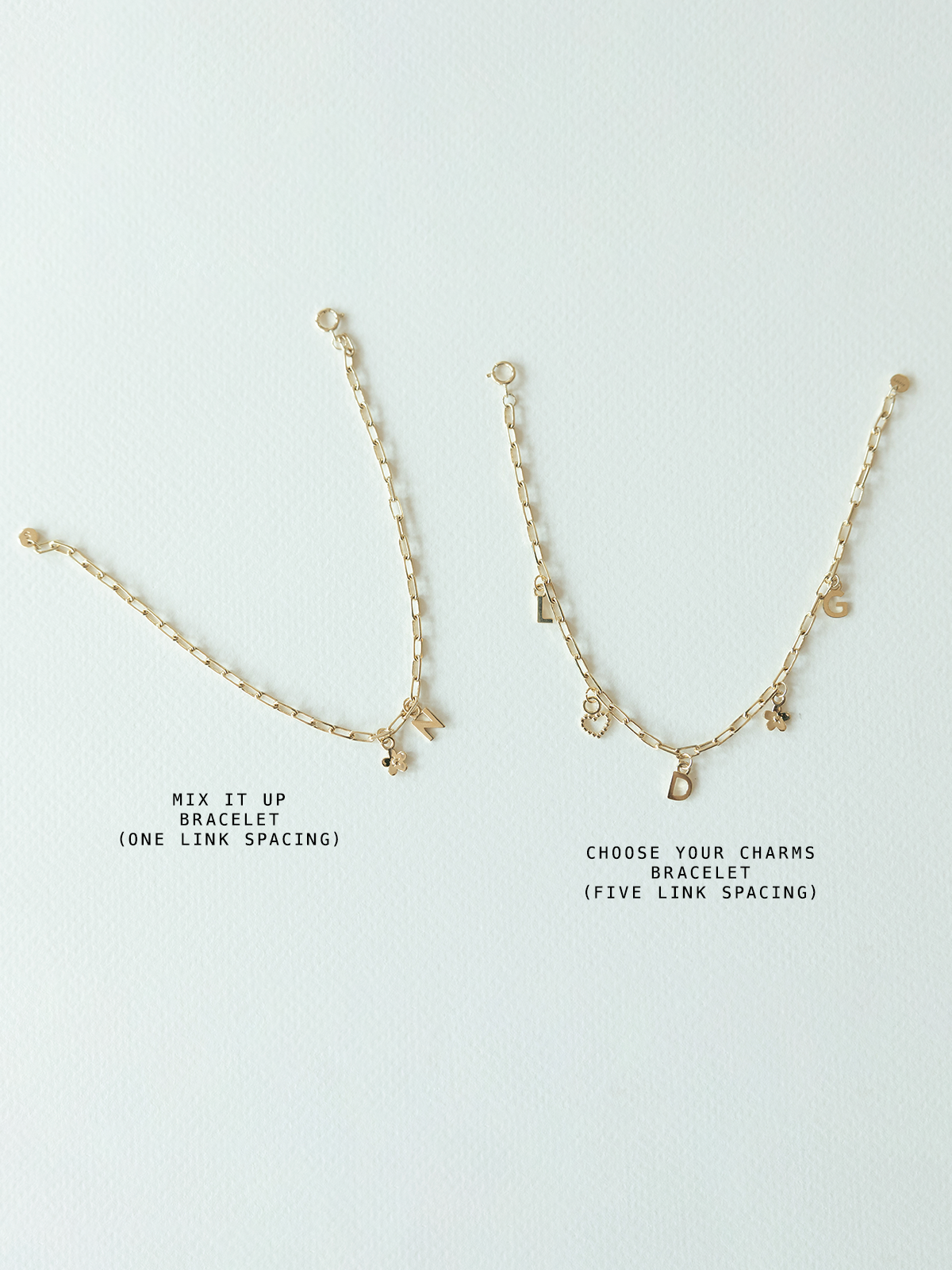 Two  solid gold bracelets with charms on a light gray background - this is comparing the mix it up bracelet on mini links chain (one link spacing between charms) and choose your charms bracelet (five link spacing between charms)