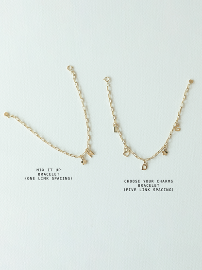 Two  solid gold bracelets with charms on a light gray background - this is comparing the mix it up bracelet on mini links chain (one link spacing between charms) and choose your charms bracelet (five link spacing between charms)