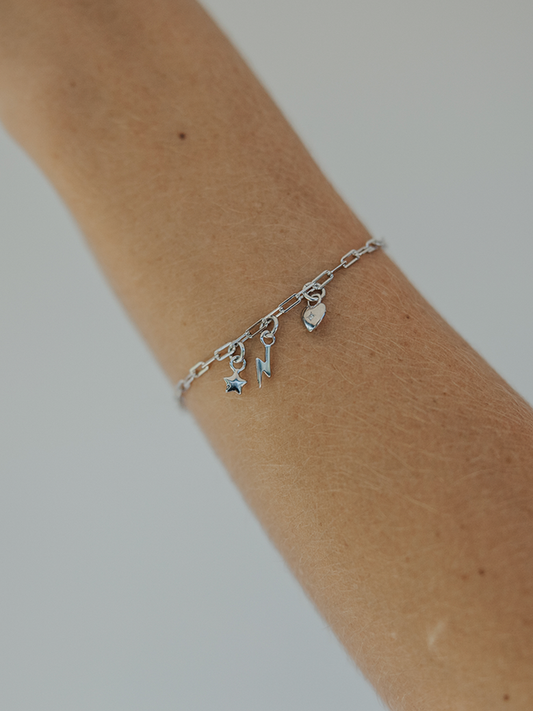 Silver bracelet with charms on a wrist against a neutral background