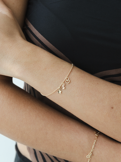 Gold bracelet with charms on a wrist against a dark background