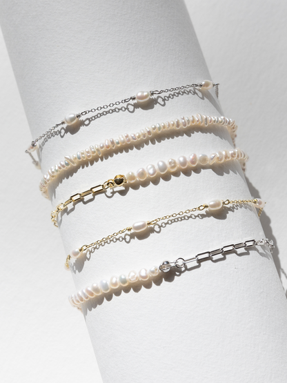 Set of pearl and chain bracelets on a white prop