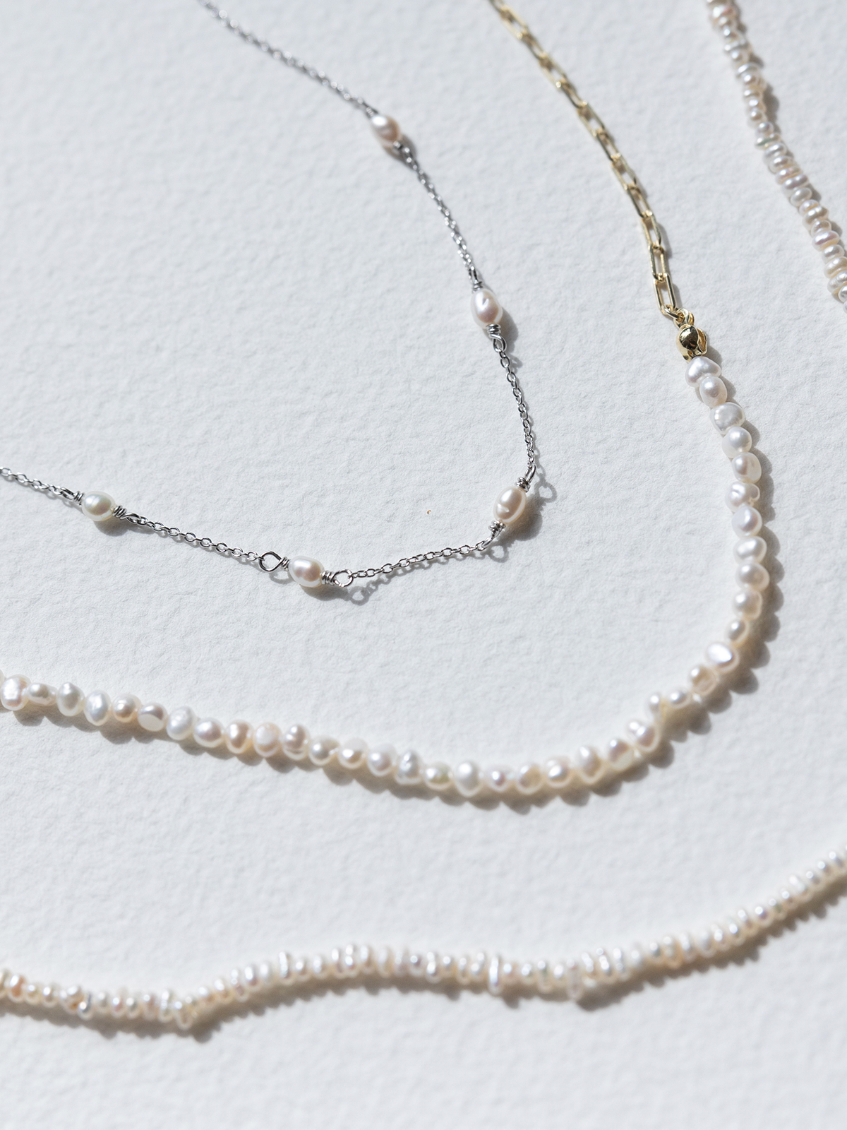 Three pearl necklaces of different lengths on a light gray background