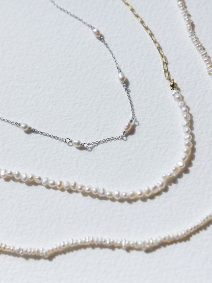 Three pearl necklaces of different lengths on a light gray background