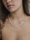 Close-up of a person wearing a gold necklace with pearl strands, showing measurements.