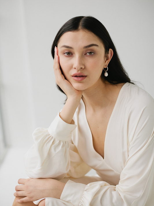 Woman wearing a white blouse with puffed sleeves against a light background wearing pearl hoop huggies earrings