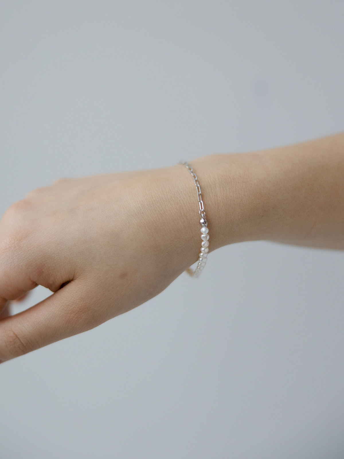 Hand wearing a pearl bracelet on a plain background
