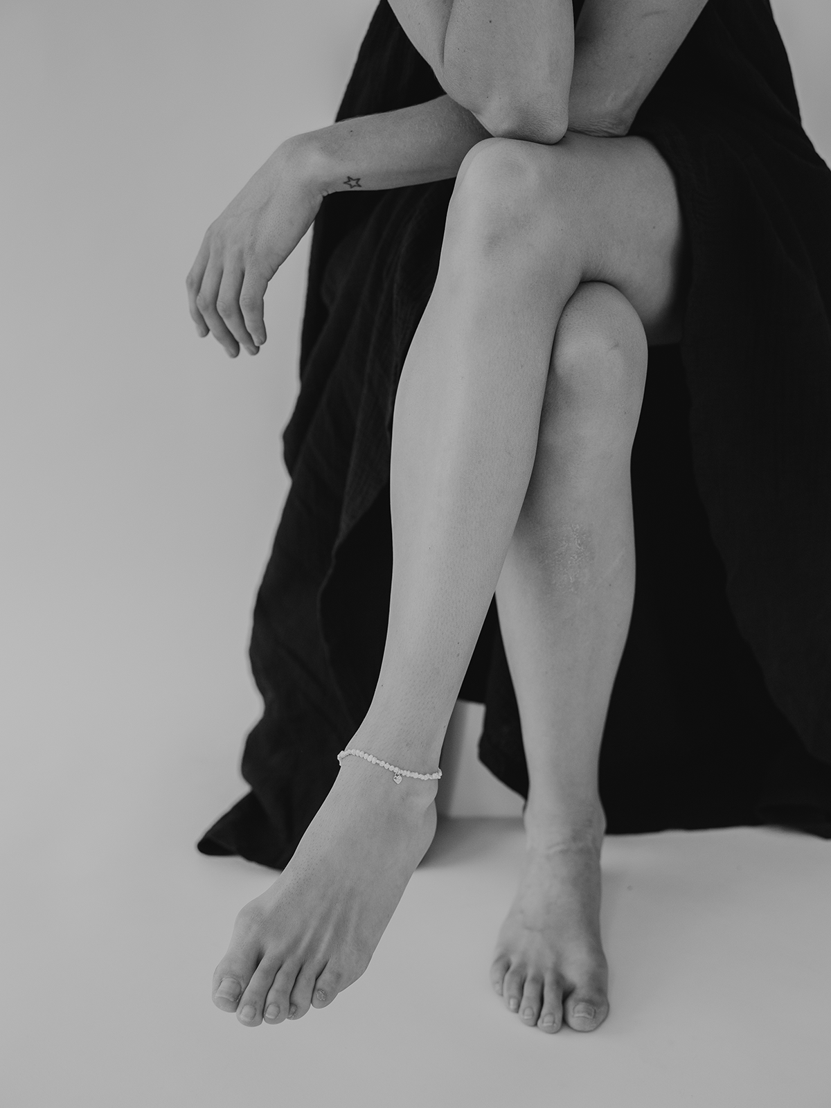 Person sitting wearing a black dress and showing the pearl anklet on her foot