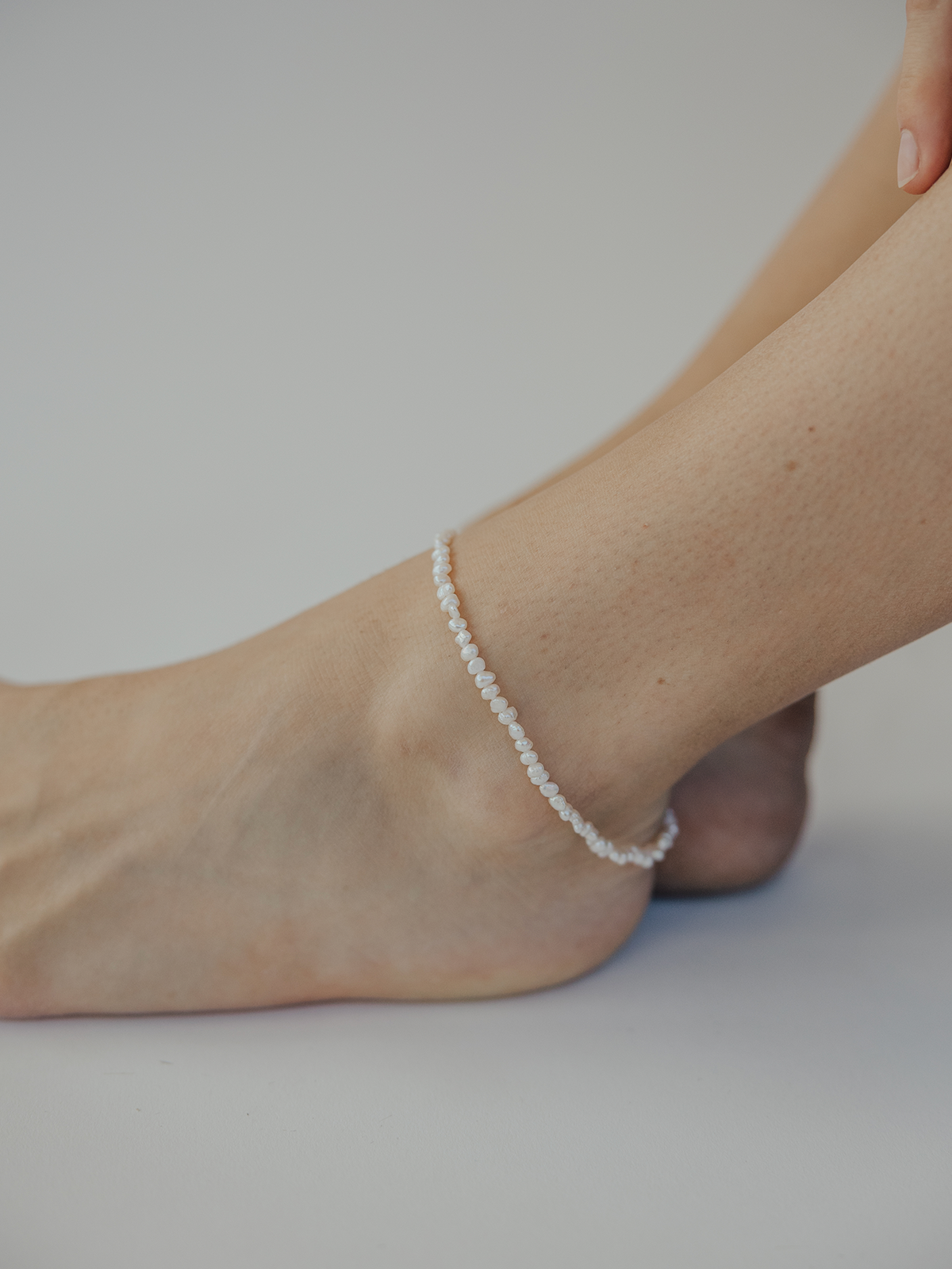 Pearl anklet on a foot against a plain background