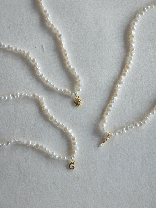 Three pearl necklaces with gold pendants on a light gray background