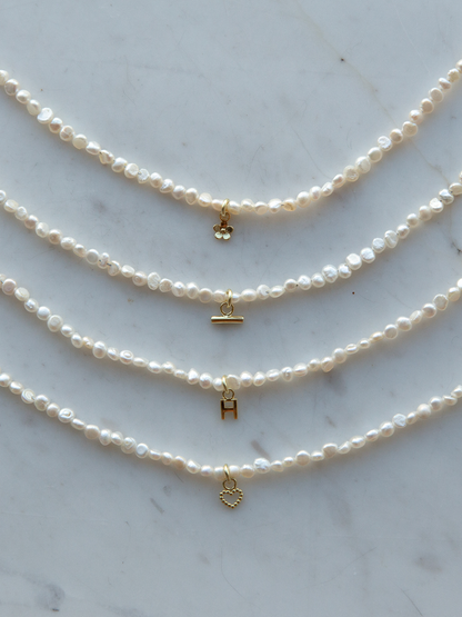 Four pearl necklaces with gold charms on a marble surface