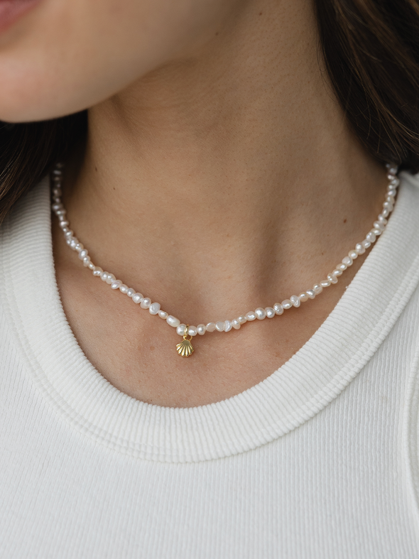 Pearl necklace with a gold charm worn by a person in a white shirt