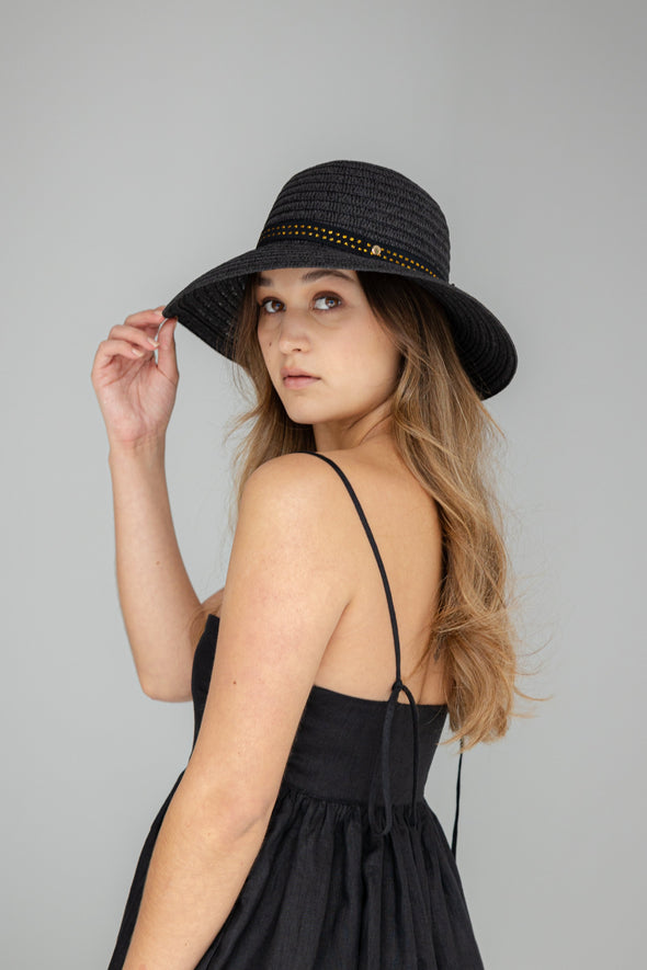 Woman wearing a black dress and hat against a gray background