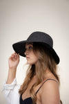 Woman wearing a black straw hat against a plain background