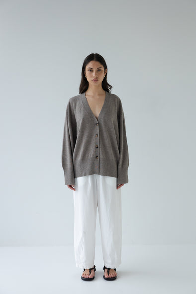 Person wearing a gray cardigan and white pants on a plain background
