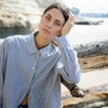 Woman sitting on a log by a body of water with cliffs in the background
