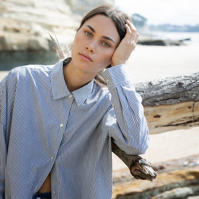 Woman sitting on a log by a body of water with cliffs in the background