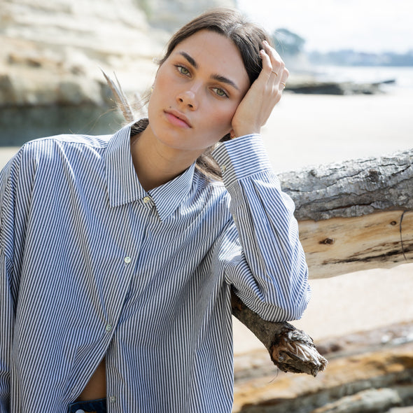 Woman sitting on a log by a body of water with cliffs in the background