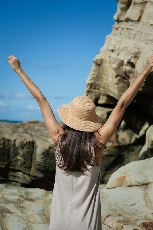 Woman with arms raised in front of a rocky cliff and clear blue sky