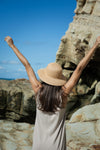 Woman with arms raised in front of a rocky cliff and clear blue sky