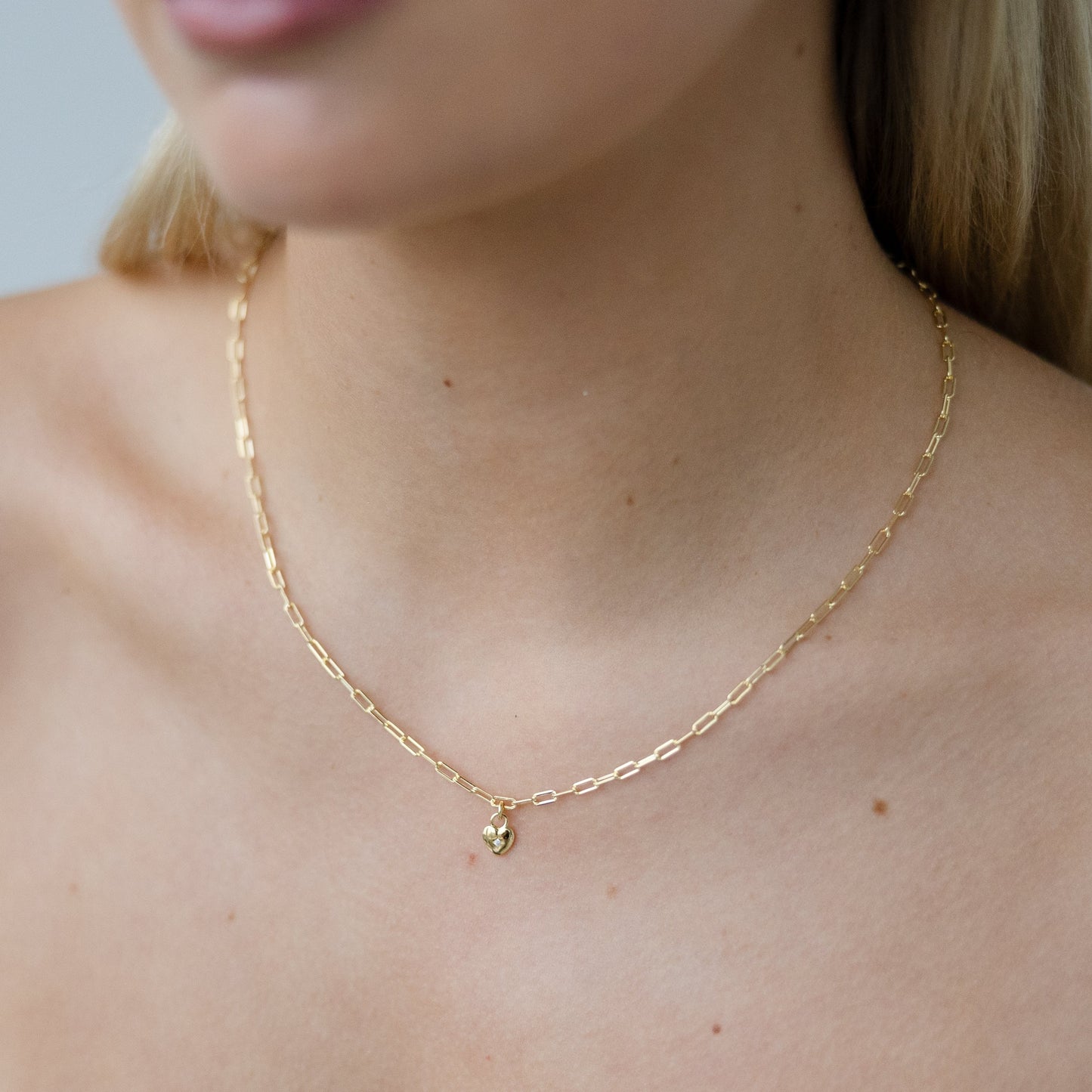 Gold necklace with a small pendant worn by a person against a neutral background