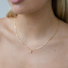 Gold necklace with a small pendant worn by a person against a neutral background