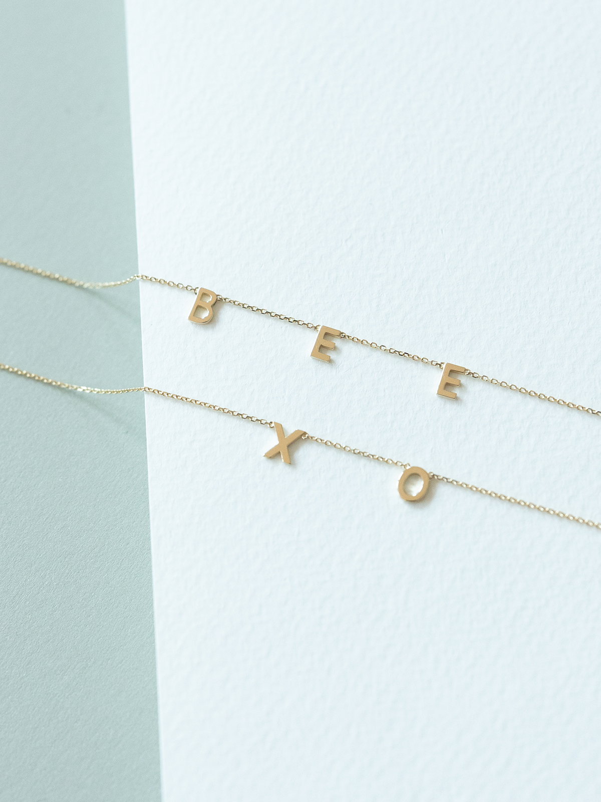 Two solid gold choose your letters bracelets on a light blue and white background