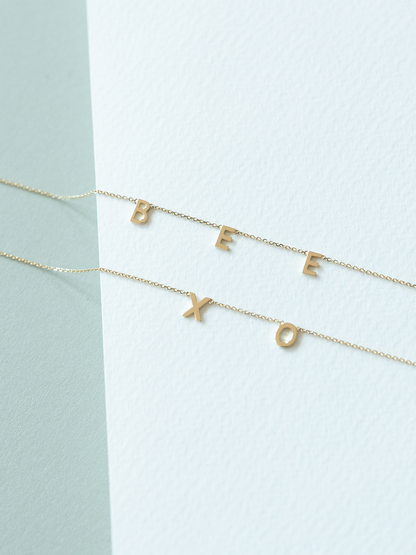 Two solid gold choose your letters bracelets on a light blue and white background